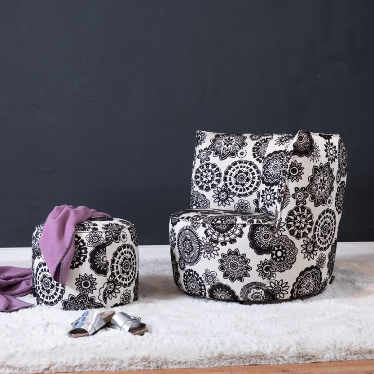 Schwarz-weiß gemusterter Sessel und Hocker auf einem weißen Teppich vor schwarzer Wand.